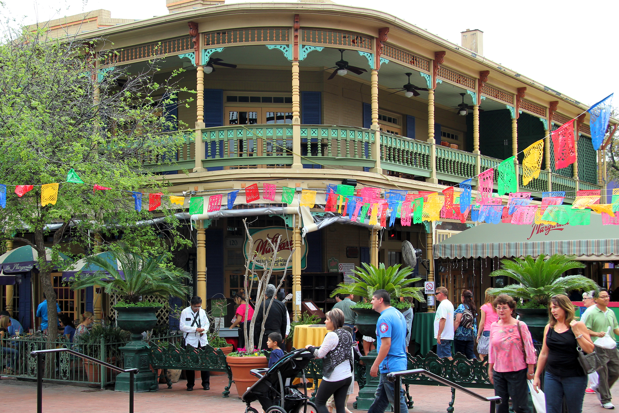 Market Square in San Antonio, Texas, with storefronts, trees, benches, and people walking through the pedestrian space